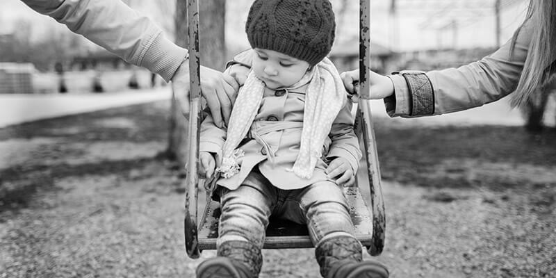 Toddler being pushed in a swing by parents