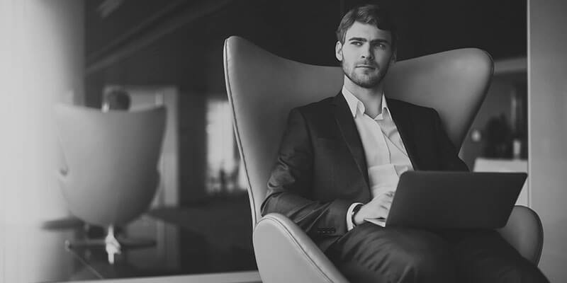 Suited millennial sat in chair with laptop