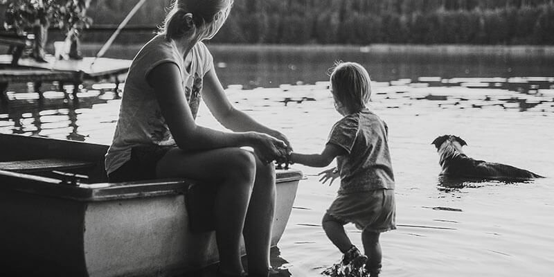 Mother sat on boat holing hands with toddler paddling in the water