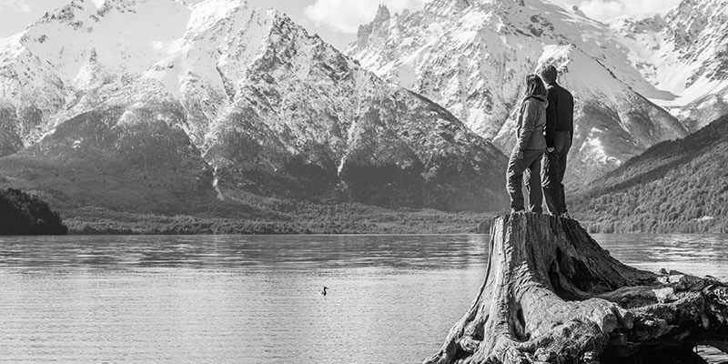 Couple stood on the edge of a lake looking out at the mountains