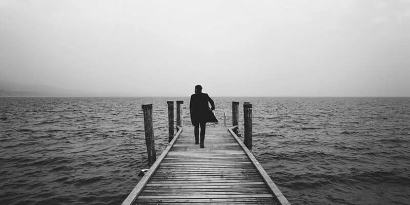 Smartly dresses man walking down a jetty towards the sea