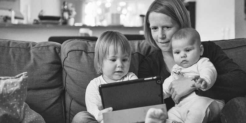 Mother, baby and toddler sat on sofa looking at tablet