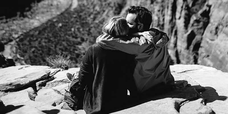 Embracing couple sat on the top of a cliff