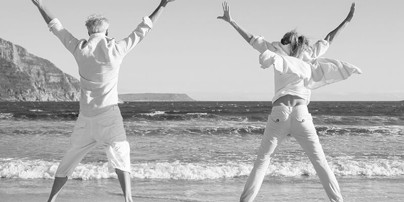 Retired couple doing star jumps on a beach