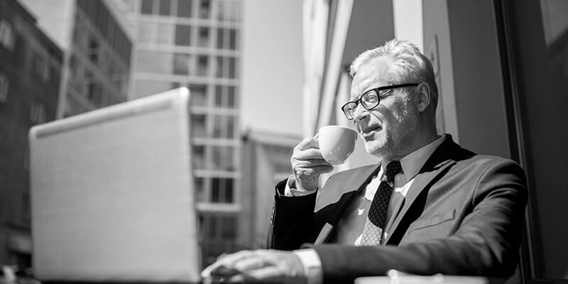 Businessman enjoying a coffee while looking at financial figures on a laptop